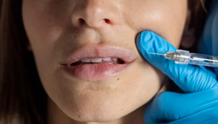 A woman's lower face receiving a cosmetic injection from a gloved hand, symbolizing non-surgical beauty treatments like Botox and fillers.