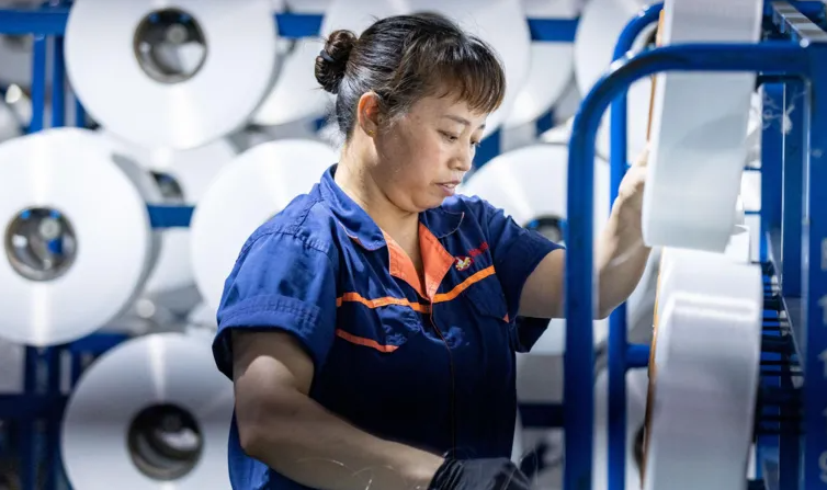 A worker operates automated spinning machinery at a textile factory in Huzhou, China, reflecting China's strong manufacturing growth in mid-2025.
